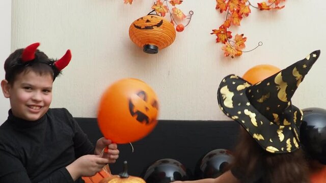 mom and daughter in fancy dress at home preparing for halloween. Girl in a witch hat. inflate balloons, prepare decorations. girl with devil horns carves bats and ghost, pumpkin