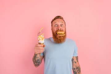 Amazed man with beard and tattoos is undecided if to eat an icecream or a sandwich with hamburger