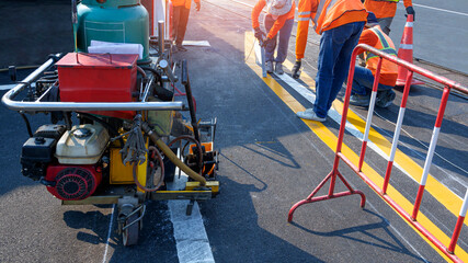 Road workers group with thermoplastic spray road marking machine are working to paint traffic lines...