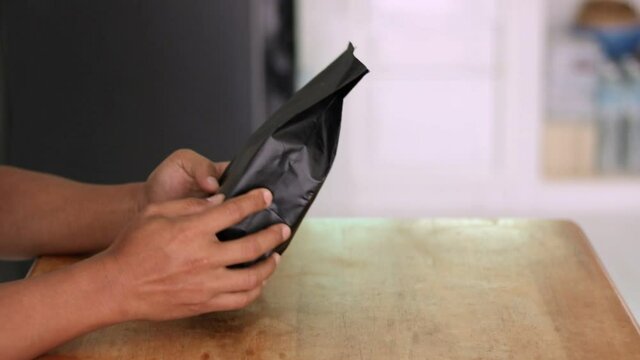 A man's hand is picking up a bag of roasted coffee beans ordered online at home.