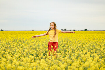 Naklejka premium Pretty long haired girl playing in vibrant canola field in full bloom