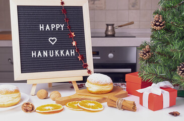 Jewish holiday of Hanukkah. A festive composition with traditional Sufganiyet donuts, fir branches and an inscription with congratulations in a cozy home kitchen. Selective focus.