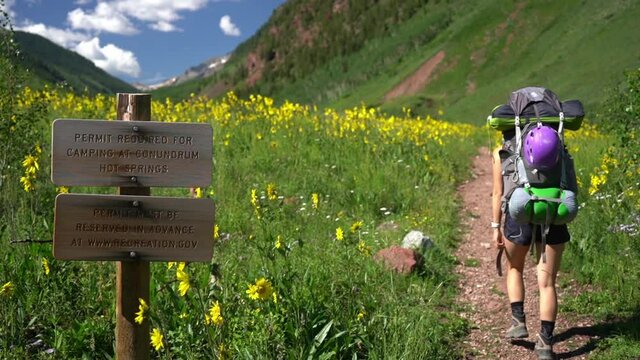 Wooden Sign on Conundrum Hot Springs Hiking Trail, Permit Required For Camping. Female Hiker and Landscape of Maroon Bells Snowmass Wilderness on Sunny Summer Day