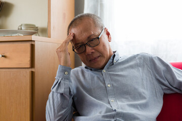 Asian senior man wearing glasses and brown and white hair having a headache while sitting in the...