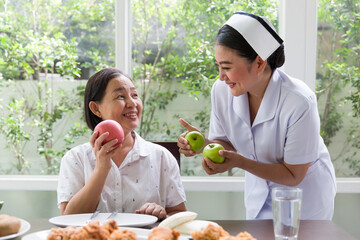 Nurse taking care or recommend senior Asian woman eating apple or fruit at home. Nurse assistant...