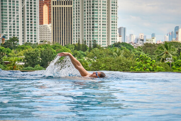 Manila, Philippines - Feb 02, 2020. A man swims a backstroke in a pool on the roof of a luxury hotel. View of the city of Manila from the pool of the luxury five-star Discovery Primea hotel.