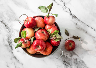 Autumn red ripe apples in a metal basket on a marble background, top view