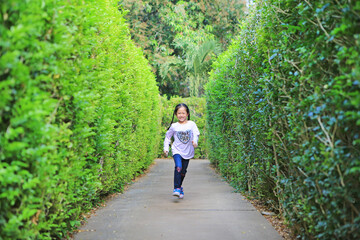 Asian child girl running in garden Maze. Kid playing in labyrinth for fun and entertainment. Back view.