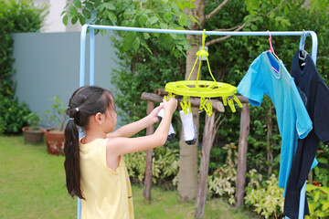 Portrait asian little kid girl putting clothespin and hangs socks to dry a clothes. Kid doing...