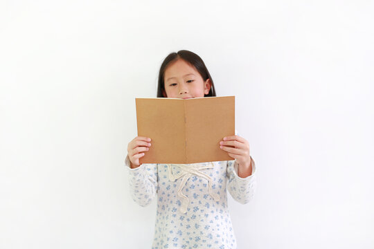 Asian Little Girl Child Holding Brown Book And Reading Over White Background.