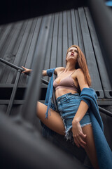 Fototapeta na wymiar Creative portrait of a red-haired woman in a short shorts and top. Design concept. Romantic portrait of young woman posing in urban area