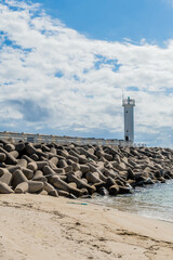 White lighthouse on end of concrete pier under blue cloudy sky.