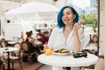 Stylish young woman eating healthy salad on a restaurant terrace, feeling happy on a summer day