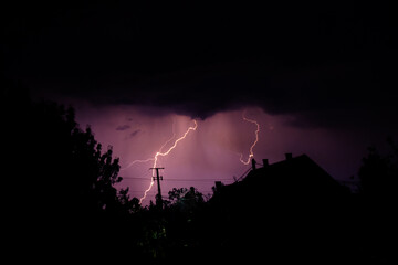 Naklejka na ściany i meble Multiple lightning strikes painting the sky purple on a summer evening during a thunderstorm