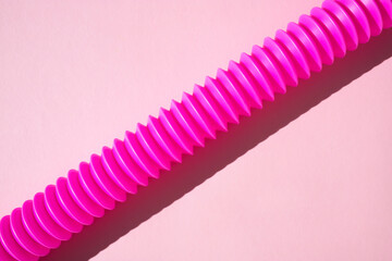 Children's anti-stress sensory plastic tube of pink color on a pink background. View from above. - obrazy, fototapety, plakaty