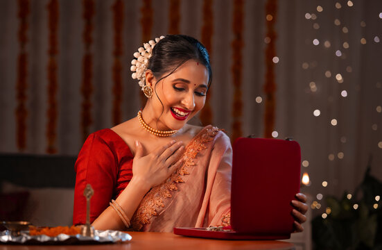 A beautiful woman opening gold jewellery box with satisfaction amidst diwali decoration, lights and a pooja thali.