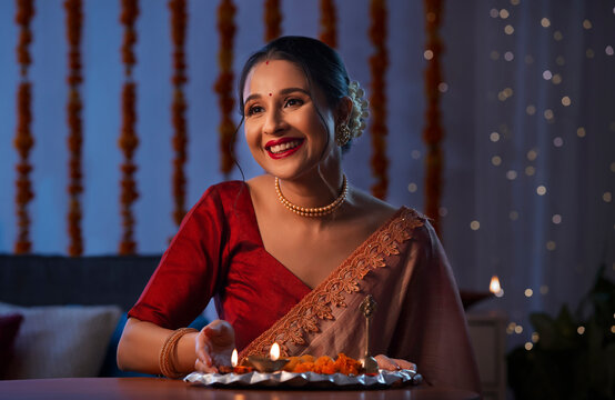 A beautiful woman with hand beside diya smiling amidst diwali decoration, lights and a pooja thali.