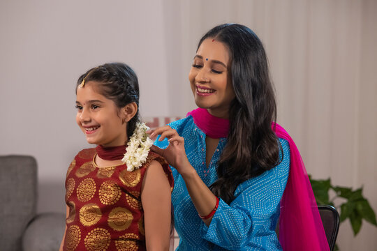 A mother adoring her daughter dressed in traditional wear by applying gajra in her hair.