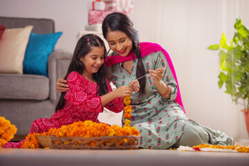 Indian girl learning flower garland composing from her mother on festival
