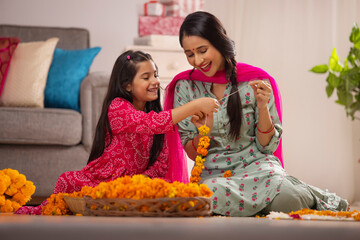 Daughter helping her mother while composing flower garland on  festival