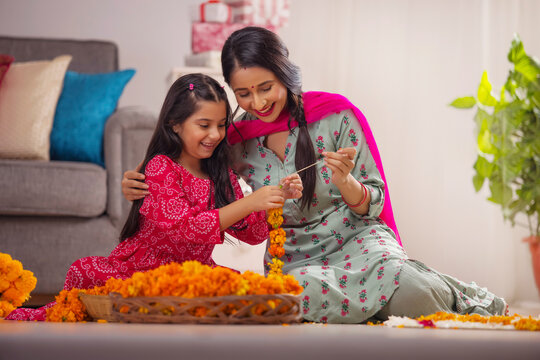 Indian girl learning flower garland composing from her mother on festival