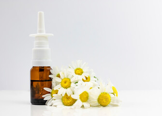 Obraz na płótnie Canvas Nasal spray and natural chamomile on a white background. Treating seasonal allergies. Banner, side view, place for text.