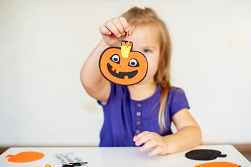 Blonde little girl created decorations for Halloween party. Cute toddler preparing for holiday Halloween. Holiday art activities, Easy felt crafts for beginners. Children's art project 