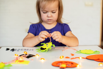 Blonde little girl created decorations for Halloween party. Cute toddler preparing for holiday Halloween. Holiday art activities, Easy felt crafts for beginners. Children's art project 