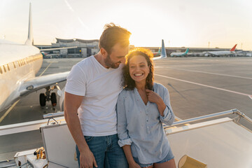 Happy man hugging pretty woman before flying on an airplane at sunset. Travel concept