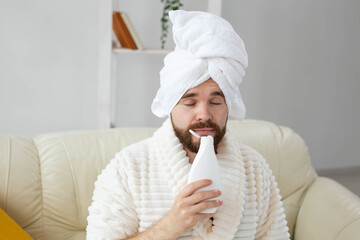 Bearded male with towel on his head applying body lotion cream. Guy smile when smell lotion cream on hand. Spa, body and skin care for man concept