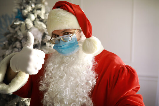 Real Santa Claus and christmas tree on a background, wearing a protective mask, glasses and hat. Christmas with social distance. Covid-19