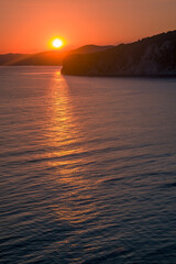 colorful sunset in the bright sky on the sea coast the sun sets behind the mountains in the bay sun reflections on the water