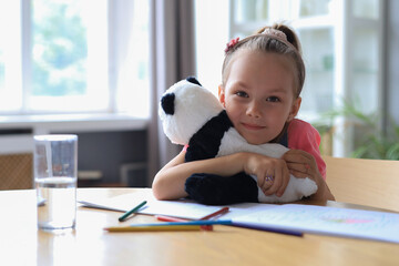 Excited child looking at camera hugging her toy panda while sitting in living room at home. © ty