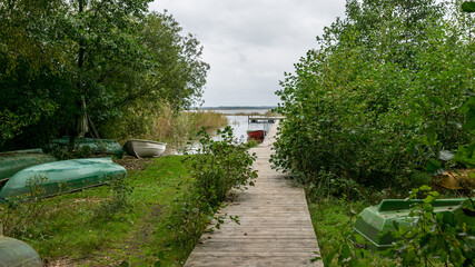 Fototapeta premium the wooden footbridge on the lake shore, fishing boats