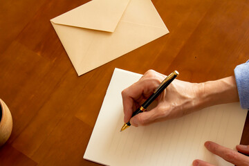テーブルに置かれた便箋と封筒とボールペンとコーヒーとペンを持つ手 - obrazy, fototapety, plakaty