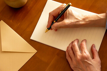 テーブルに置かれた便箋と封筒とボールペンとコーヒーとペンを持つ手 - obrazy, fototapety, plakaty