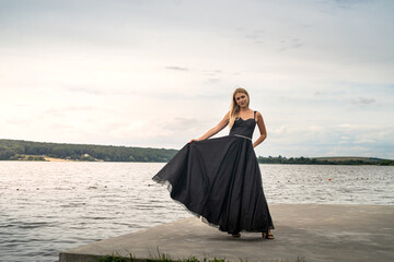 Beautiful young woman in evening long black dress near pond