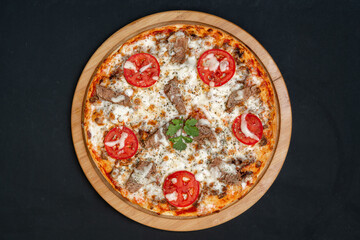 Pizza with meat and tomatoes on black background, top view.