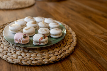 Fototapeta na wymiar White and pink macarons lie on a plate on a wooden table. Delicious light cookies on a brown background. Bakery. Valentine's Day background