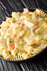 Chicken a la King is a dish consisting of diced chicken in a cream sauce with sherry, mushrooms, and vegetables served over noodles close up in the plate on the table. Vertical