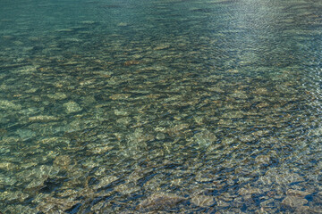 Beautiful nature background of stony bottom in turquoise transparent water of glacial lake in sunlight. Sunny backdrop with many stones in green clear water of glacier lake. Texture of mountain lake.