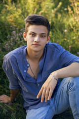 Naklejka na ściany i meble sexy teen guy sitting on the grass in nature in a shirt and jeans
