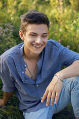 sexy teen guy sitting on the grass in nature in a shirt and jeans