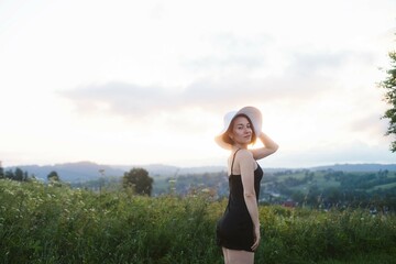 woman standing in a field, holding hat and looking at camera, space for text, atmospheric epic moment