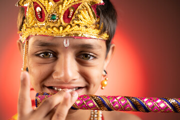 close up head shot of kid in Lord krishna costume playing flute during shri krishna Janmashtami.
