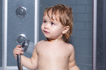 Cute baby boy enjoying bath and bathed in the bathroom. Child bathing under a shower. Funny kids face closeup.