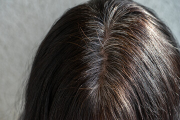 Close up of middle age caucasian woman with dark brown hair and regrown gray hair roots. View from above
