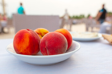 Ripe peaches in a white plate on the table.