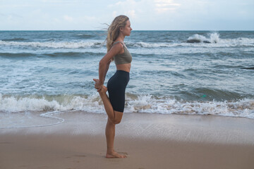 Fototapeta na wymiar fit active sexy young blonde woman in sportswear stretching legs muscles on the beach after jogging. healthy girl do gymnastics workout by the sea.