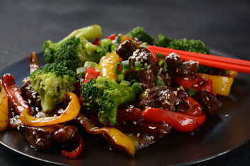 Asian teriyaki beef with red and yellow bell peppers, broccoli and sesame seeds on a plate on the table. Spicy teriyaki beef stir fry with vegetables and rice  on a dark background